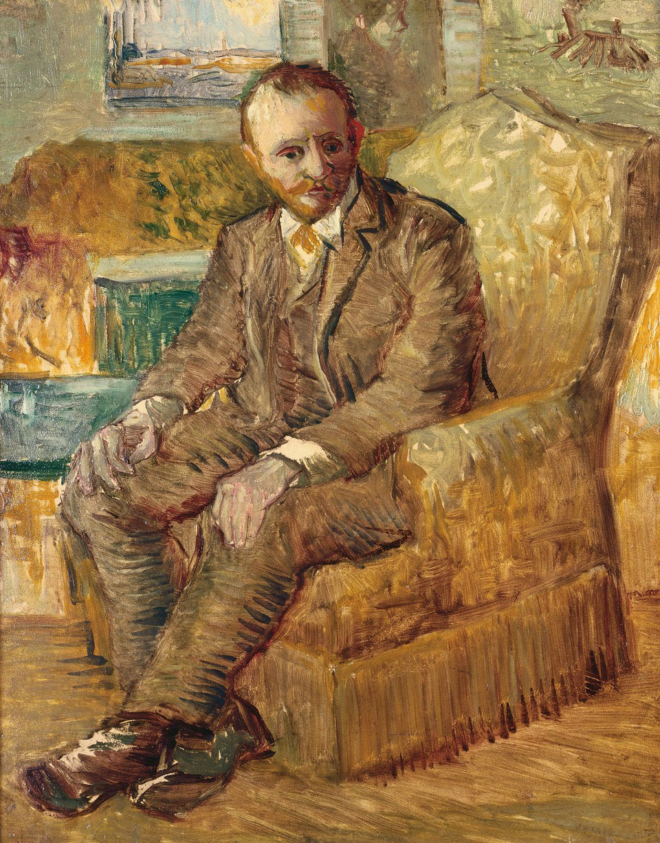 A bearded man, wearing a suit, sits in a chair.