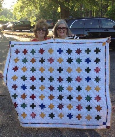 Two women smile, holding a quilt with 80 stars.