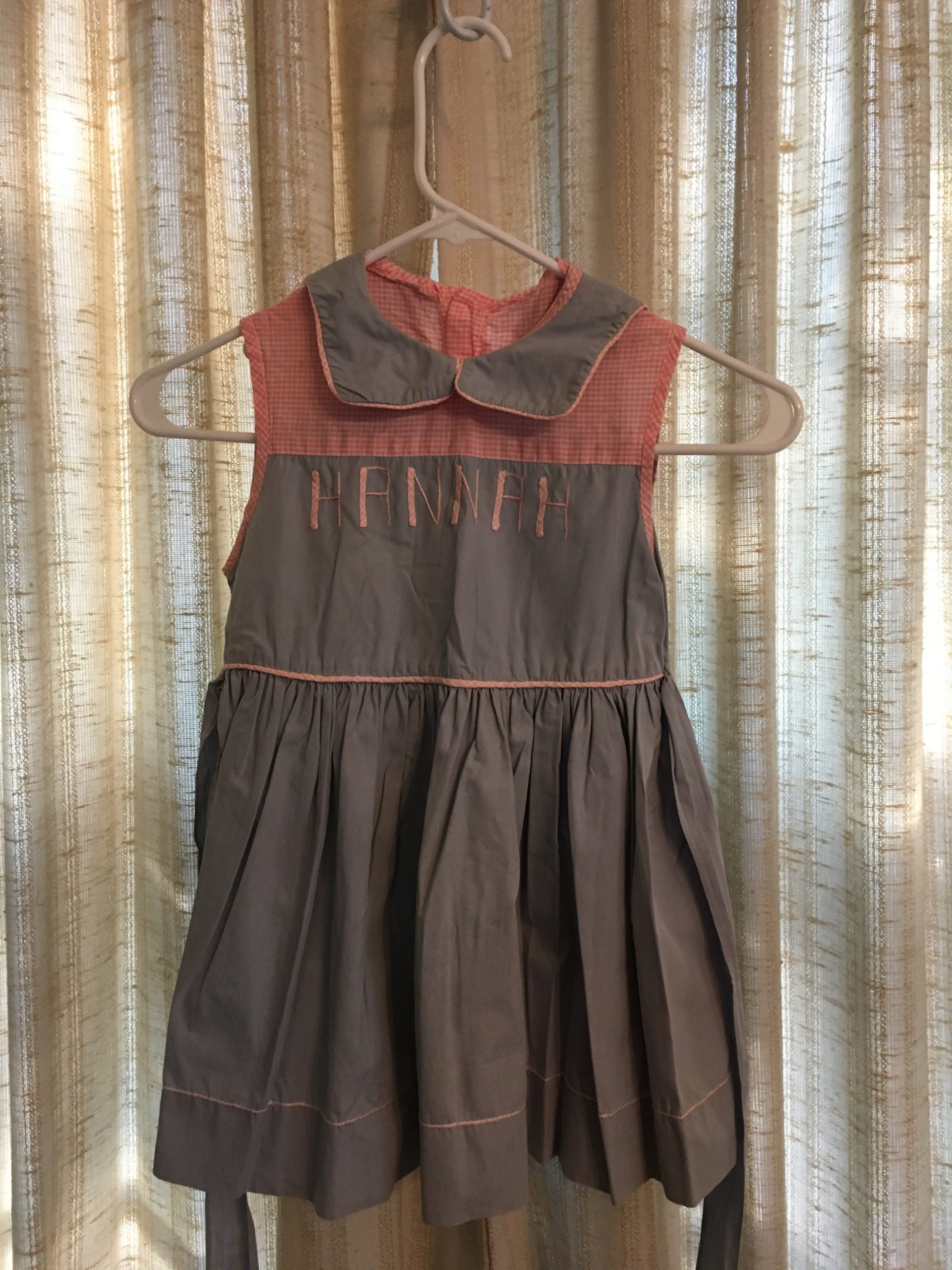 A child's dress hangs in front of a window.