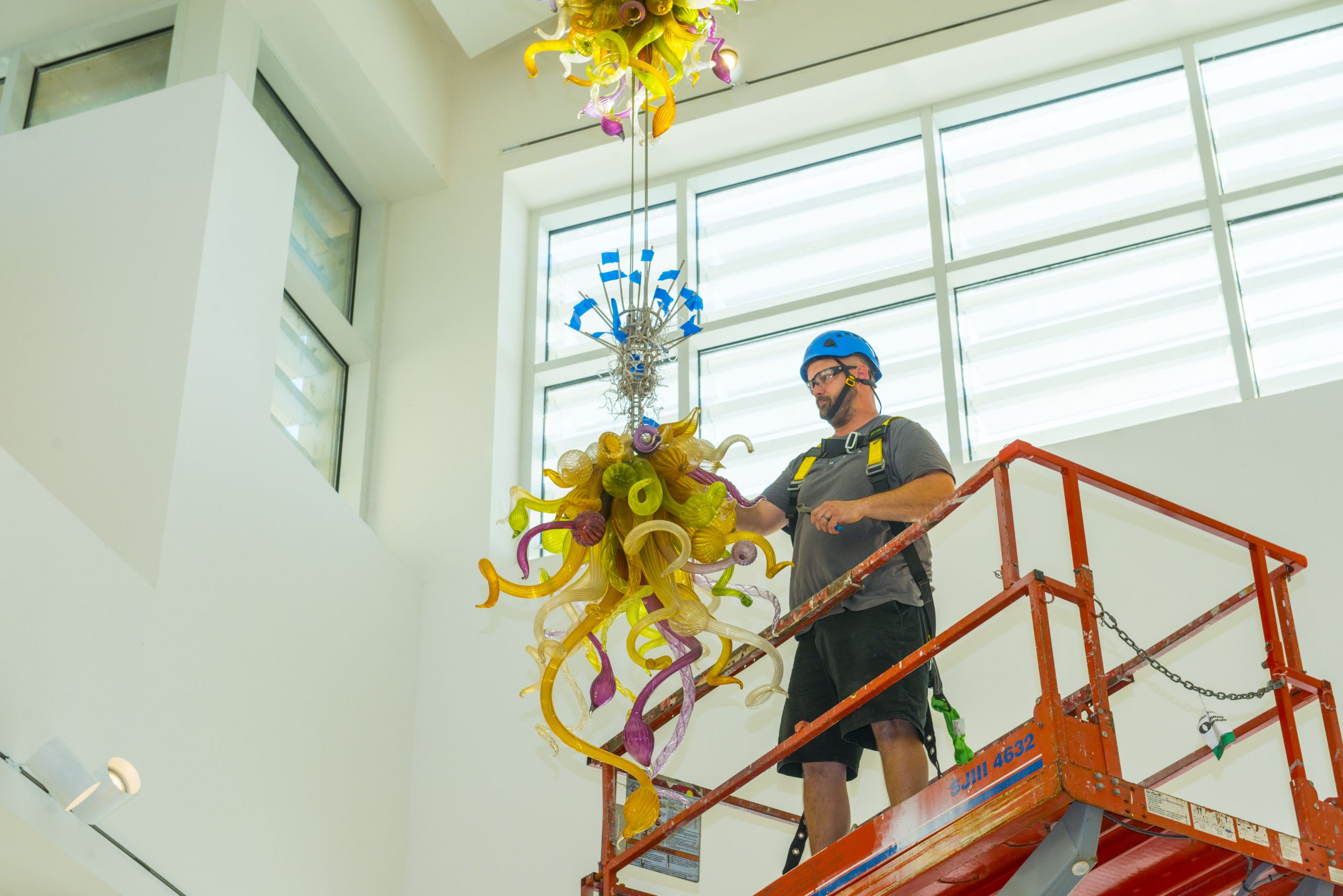 A man in safety gear standing on a lift assembles an intricate glass sculpture.