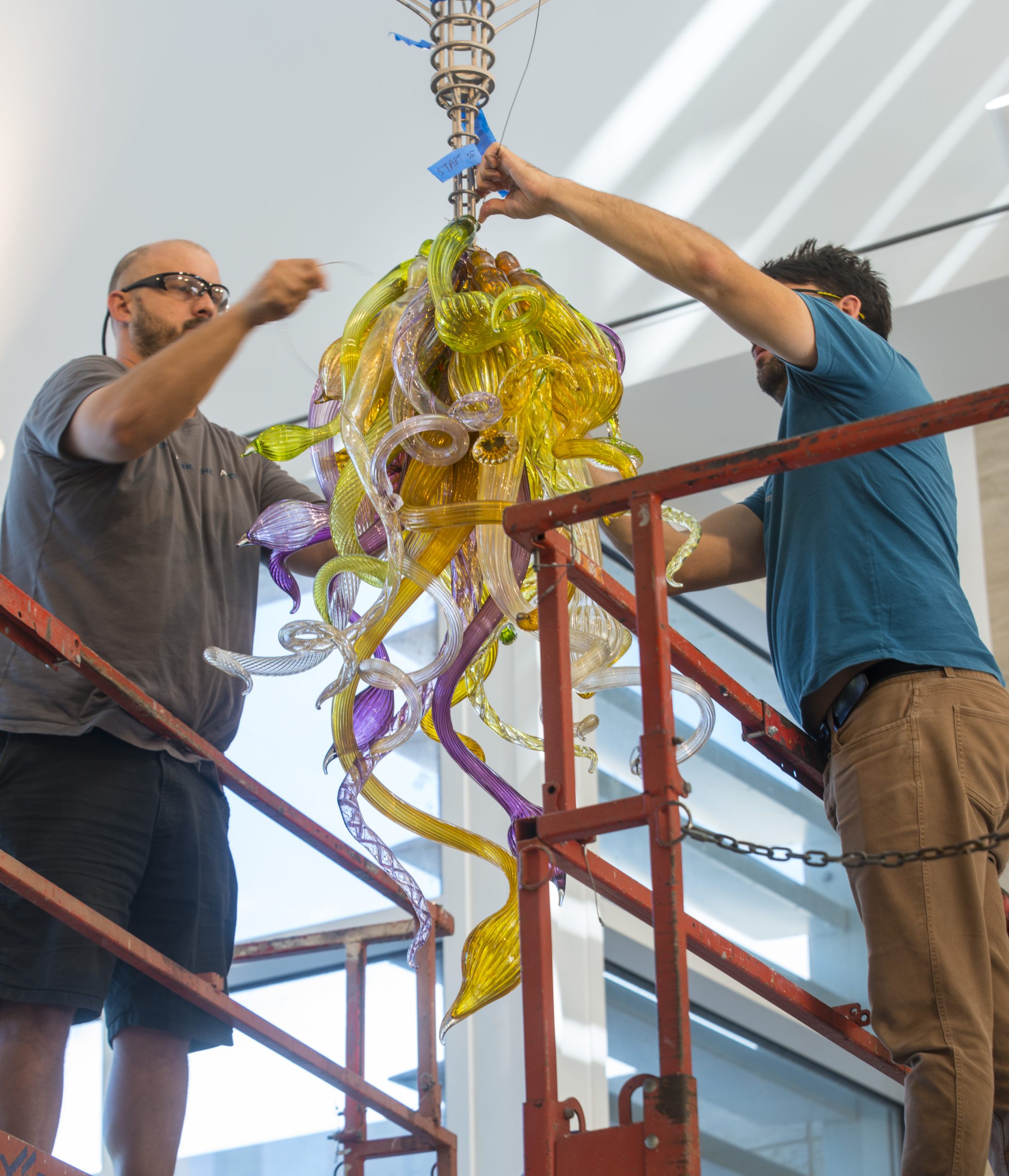 Two men disassemble an intricate glass sculpture.