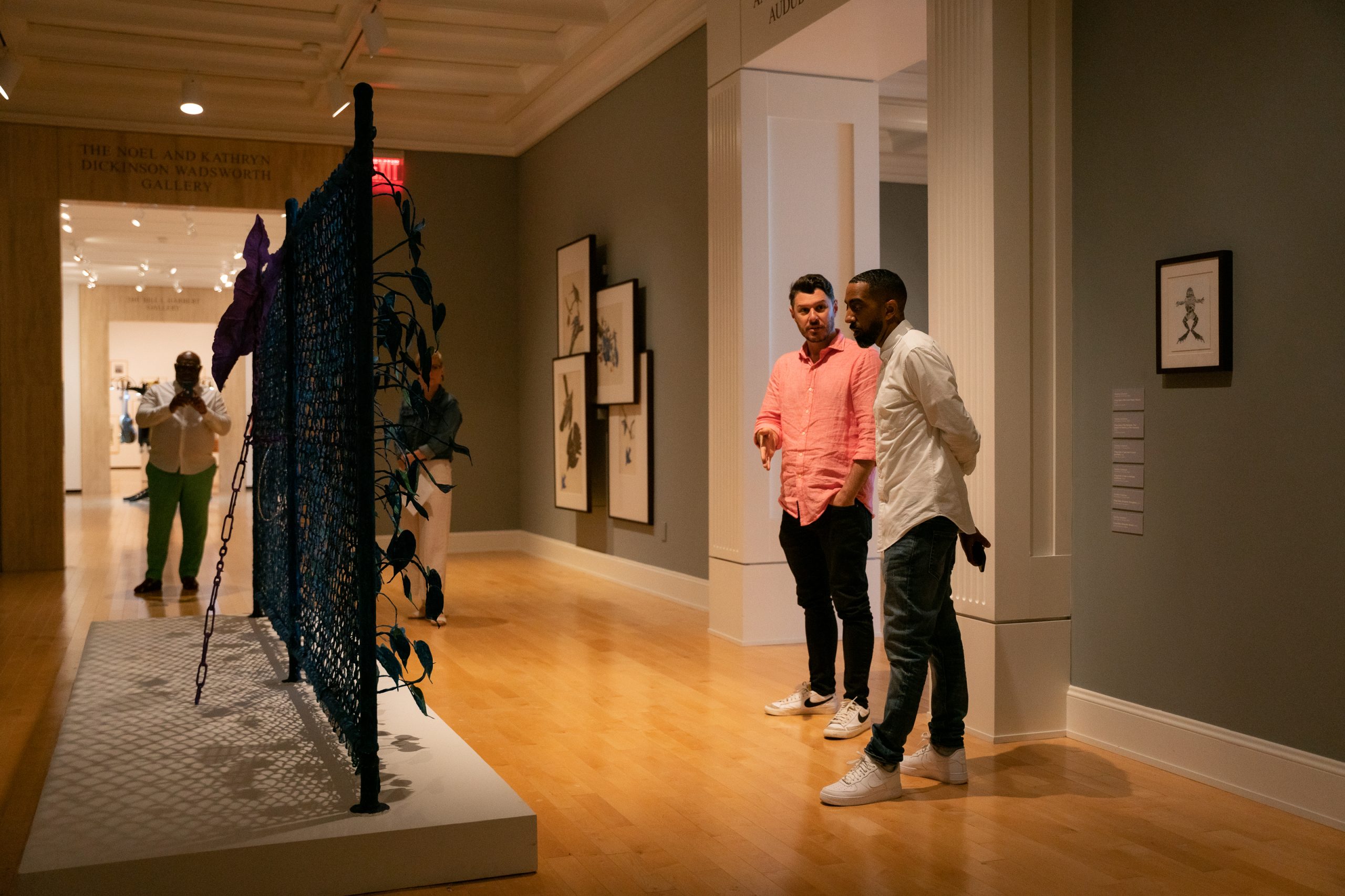Two men discuss a sculpture in the middle of a gallery.
