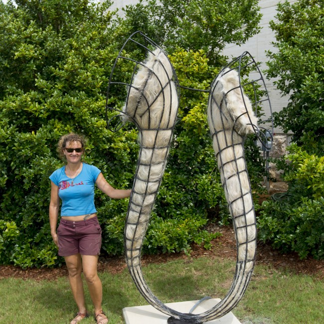 An artist poses with a Horseshoe-shaped sculpture made from artificial human hair and steel