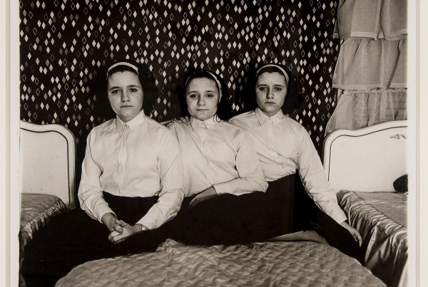 Three girls sit on a bed in a silver gelatin print.