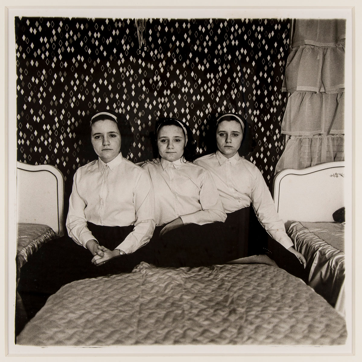 Three girls sit on a bed in a silver gelatin print.
