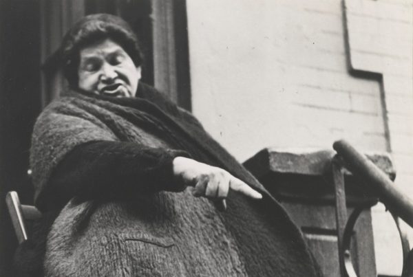 A woman sitting on a stoop gestures in this black and white photograph.