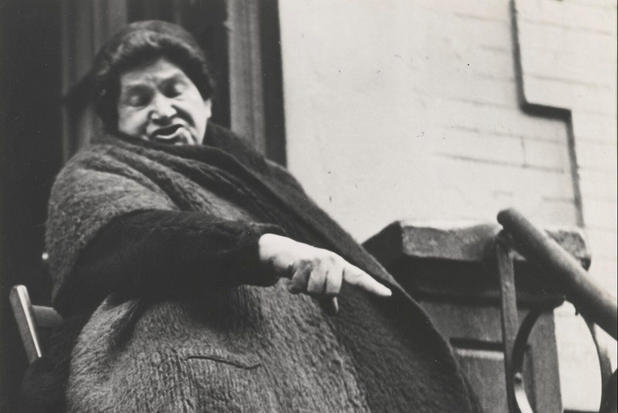 A woman sitting on a stoop gestures in this black and white photograph.