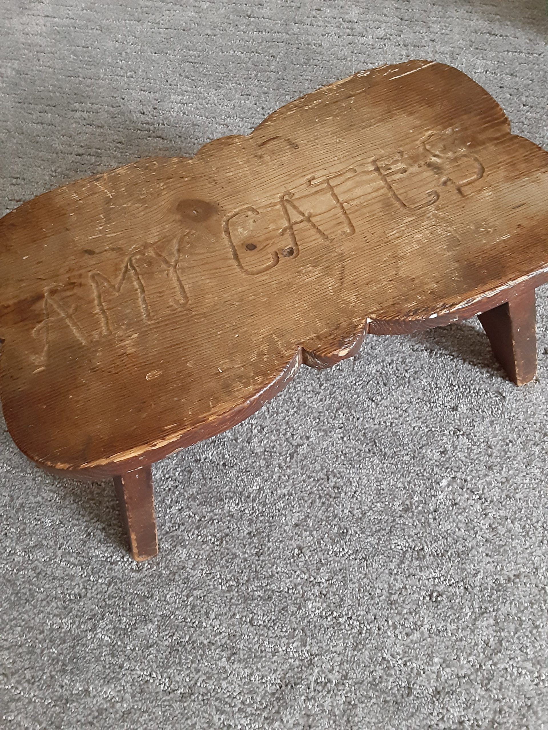 A rough and well-loved wooden footstool with the name Amy Cates carved on the top.