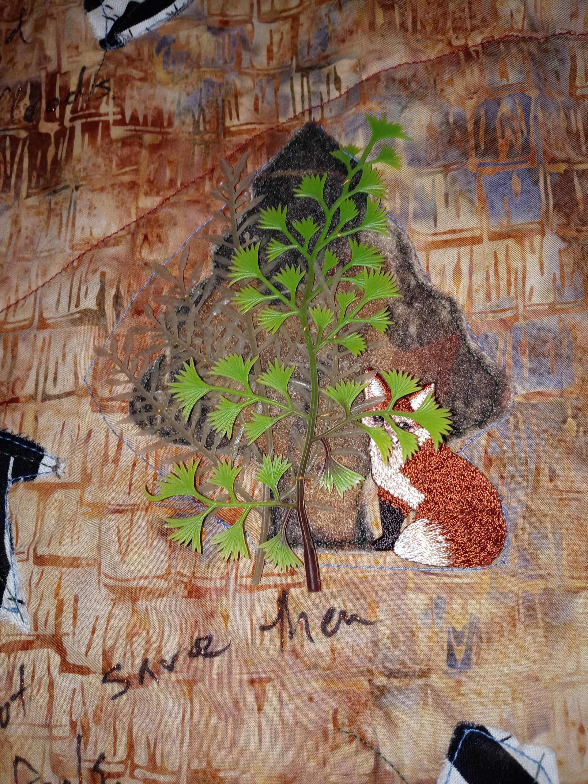 An embroidered fox hides behind a plastic toy tree on a quilt.