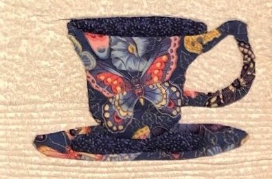 A quilted teapot with a warm and cool colored butterfly.