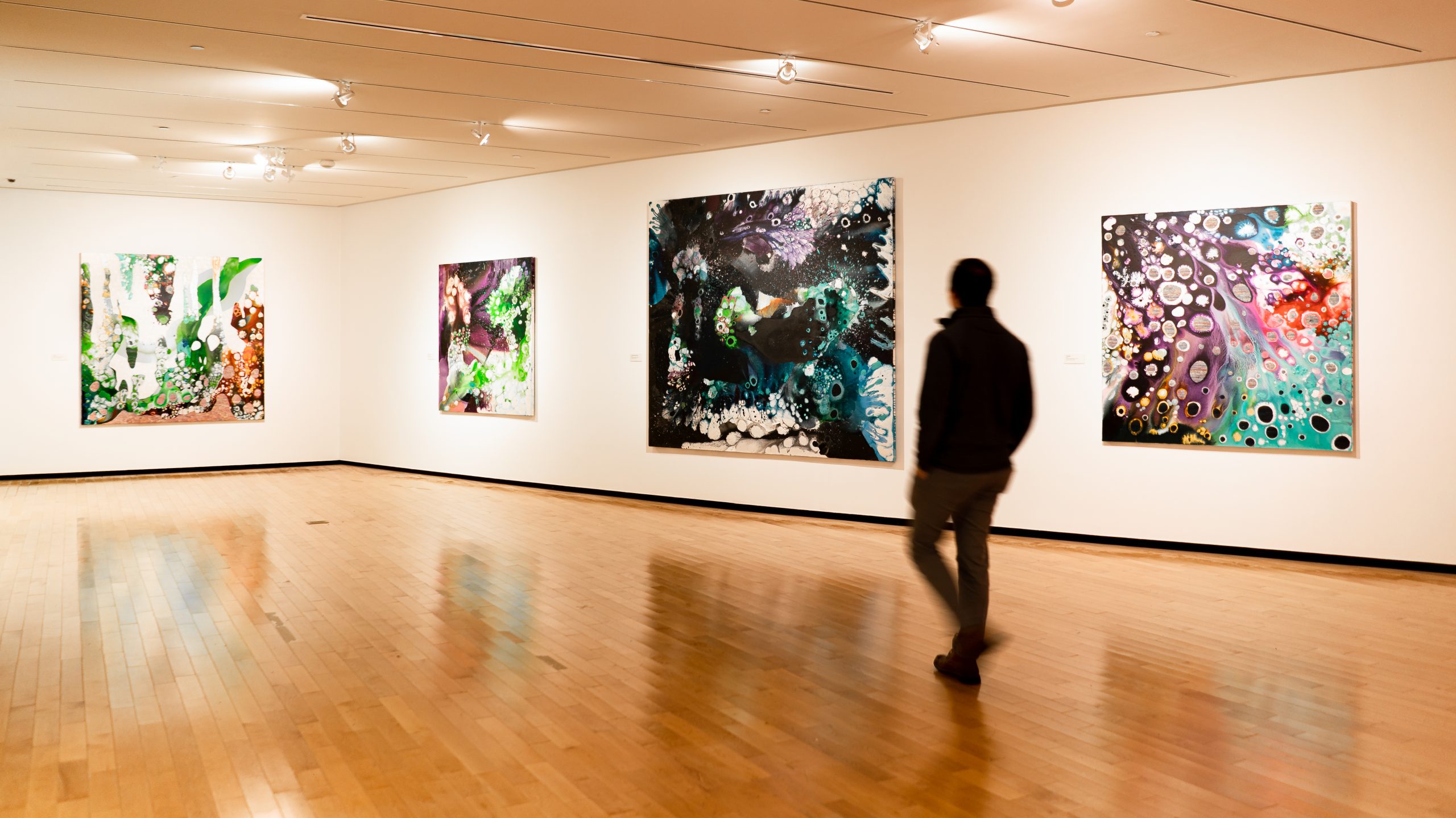 A man walks in a gallery filled with Abstract paintings.
