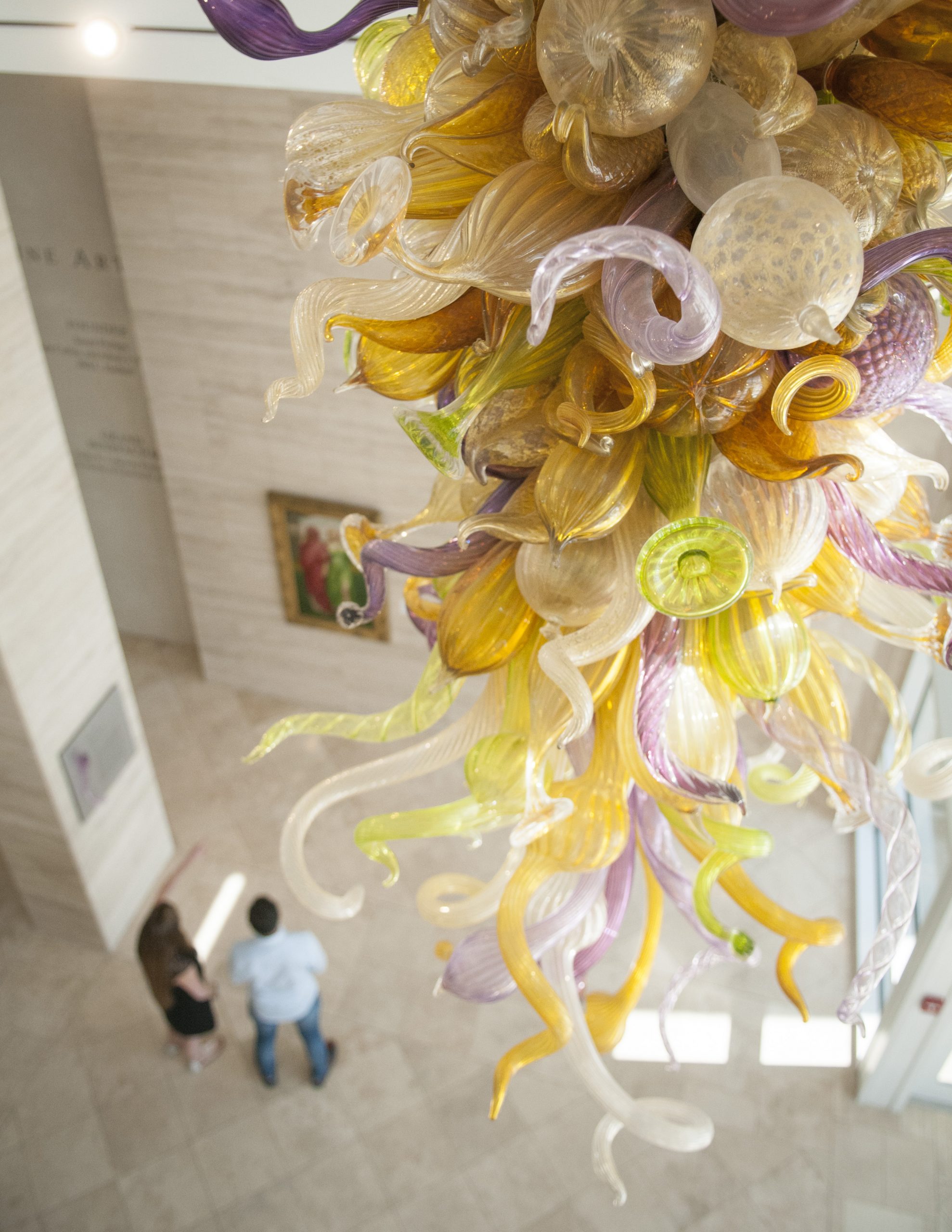 An aerial view of an intricate glass sculpture that hangs above two people.