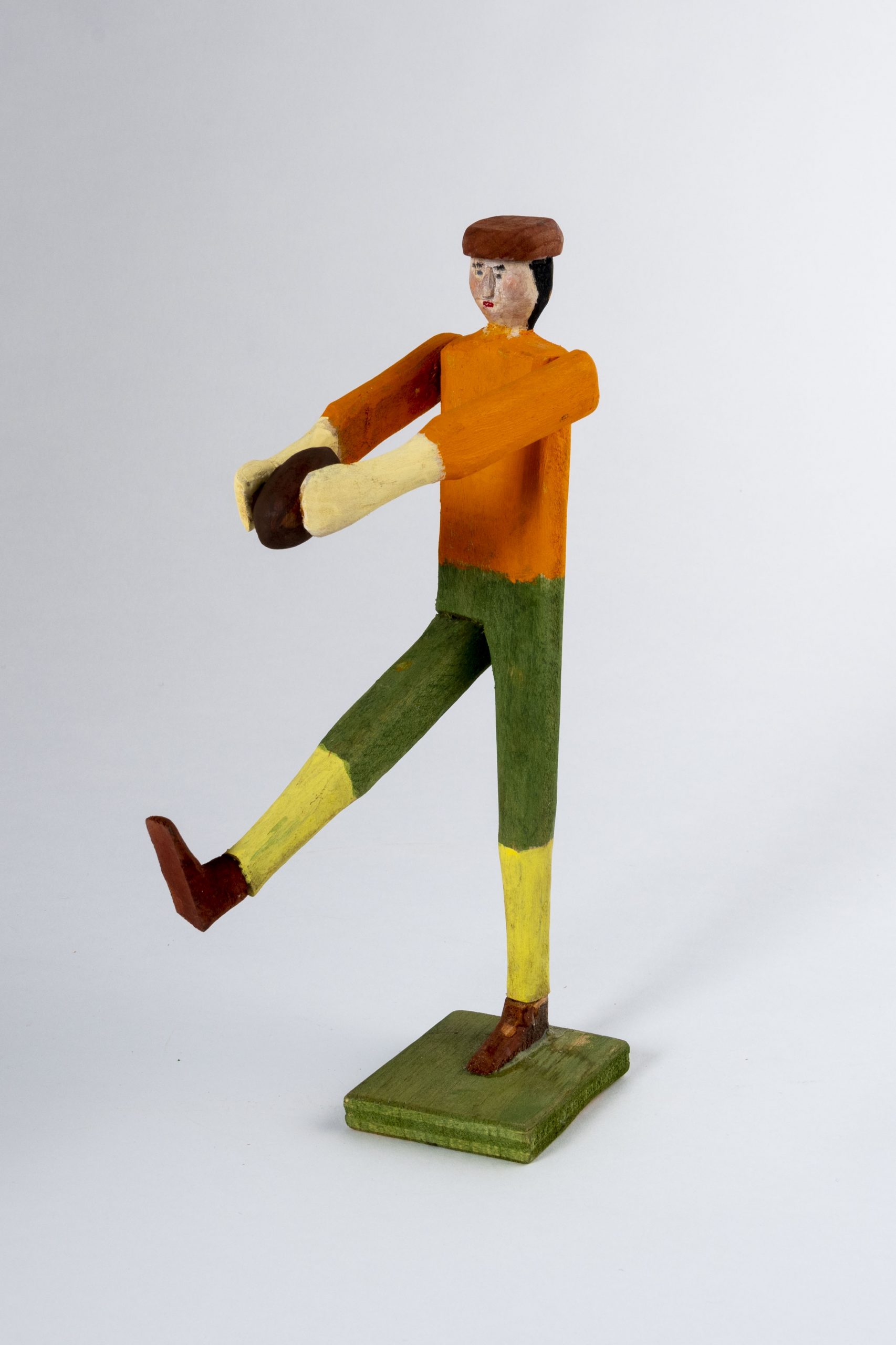 A folk art wooden sculpture of a football player kicking a ball