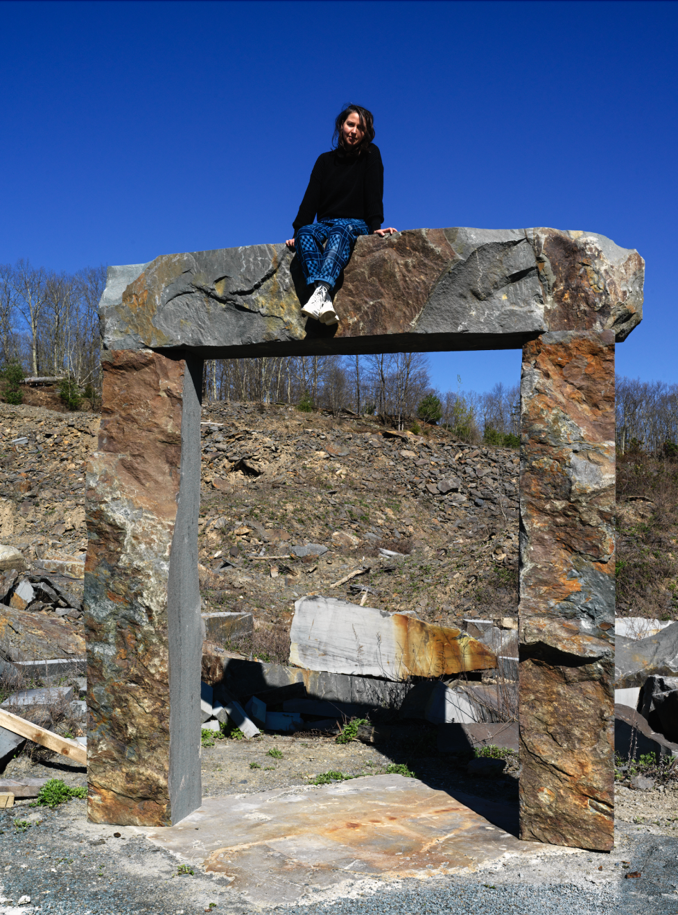 Artist Sam Moyer sits upon a stone arch.