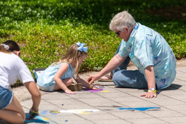 A child works on a chalk drawing with a senior citizen.