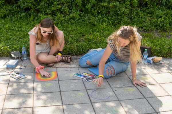 Two people draw on the sidewalk using chalk.