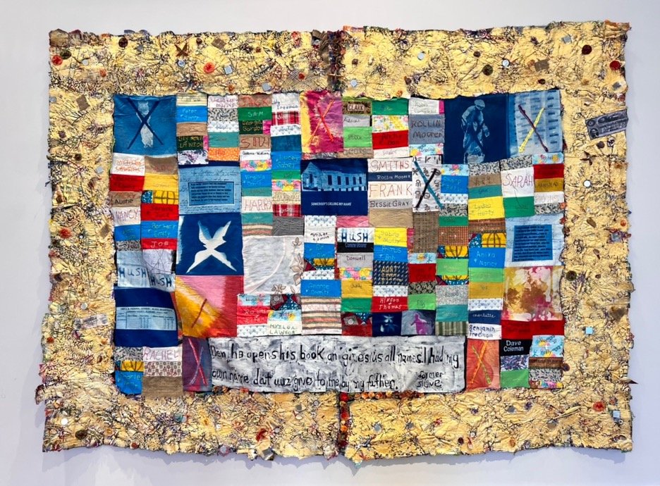 Photo of quilt made with a variety of fabrics and colors including shades of blue, yellow, pink, red, teal, green, white and purple. Some fabric pieces include names such as Sarah, Harry, and Joe. at the bottom center, a larger white fabric piece features text: "Den he opens his book an gives us all names. I had my own name dat wuz give to me by my father. Former slave." Quilt made by Wine McQueen.