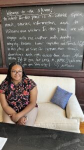 Student guide Naomi Taylor sits on an ivory couch in front of a chalkboard.