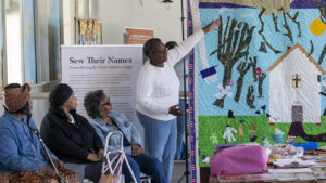 Sew Their Name attendees look on as a workshop leader discusses Yvonne Wells' quilt, "Worshippers at Mr. Willing Church."