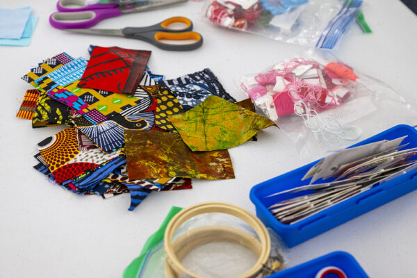 Quilting materials for participants, including bright squares of fabric, needles, scissors, and cross stitch hoops.