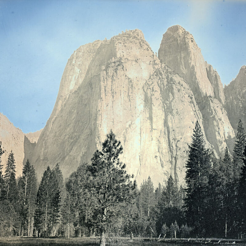 A landscape photograph. of four mountainous peaks above a forest of evergreen trees.