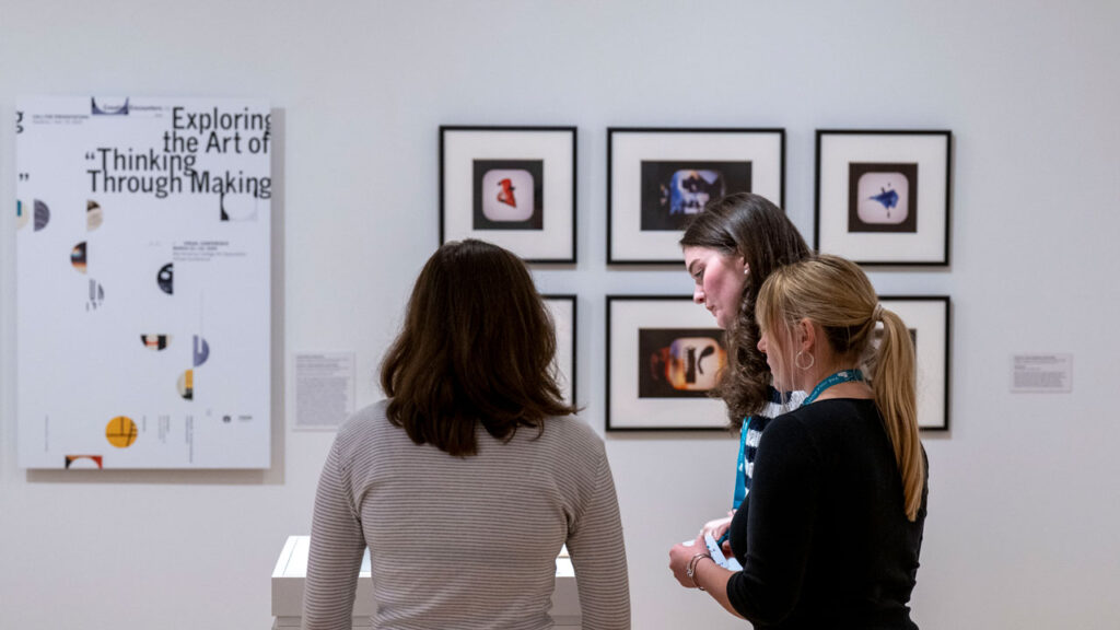 Three people examine a model in a museum gallery.