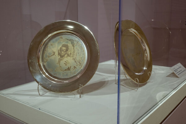 Close up shot of display cases with silver plate artworks and wall text for the exhibition, "Binh. Danh: Advancing American Art." Plates are revealed to have photographs in the center.