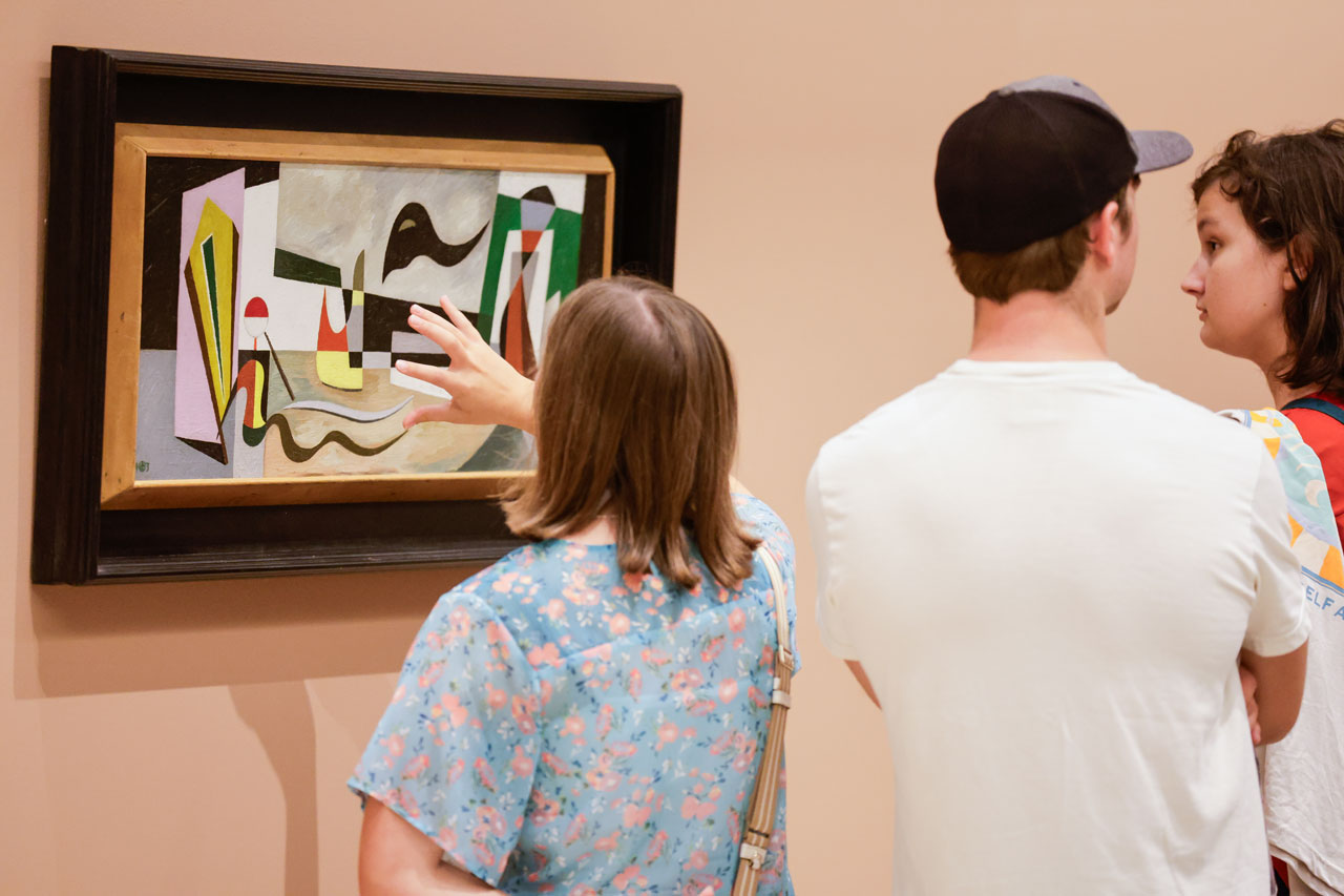 Person gestures towards painting as two other people look on.