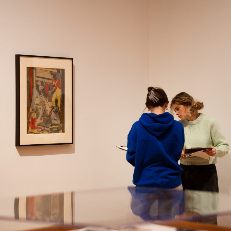 Two students confer about a 2D object in a museum gallery.