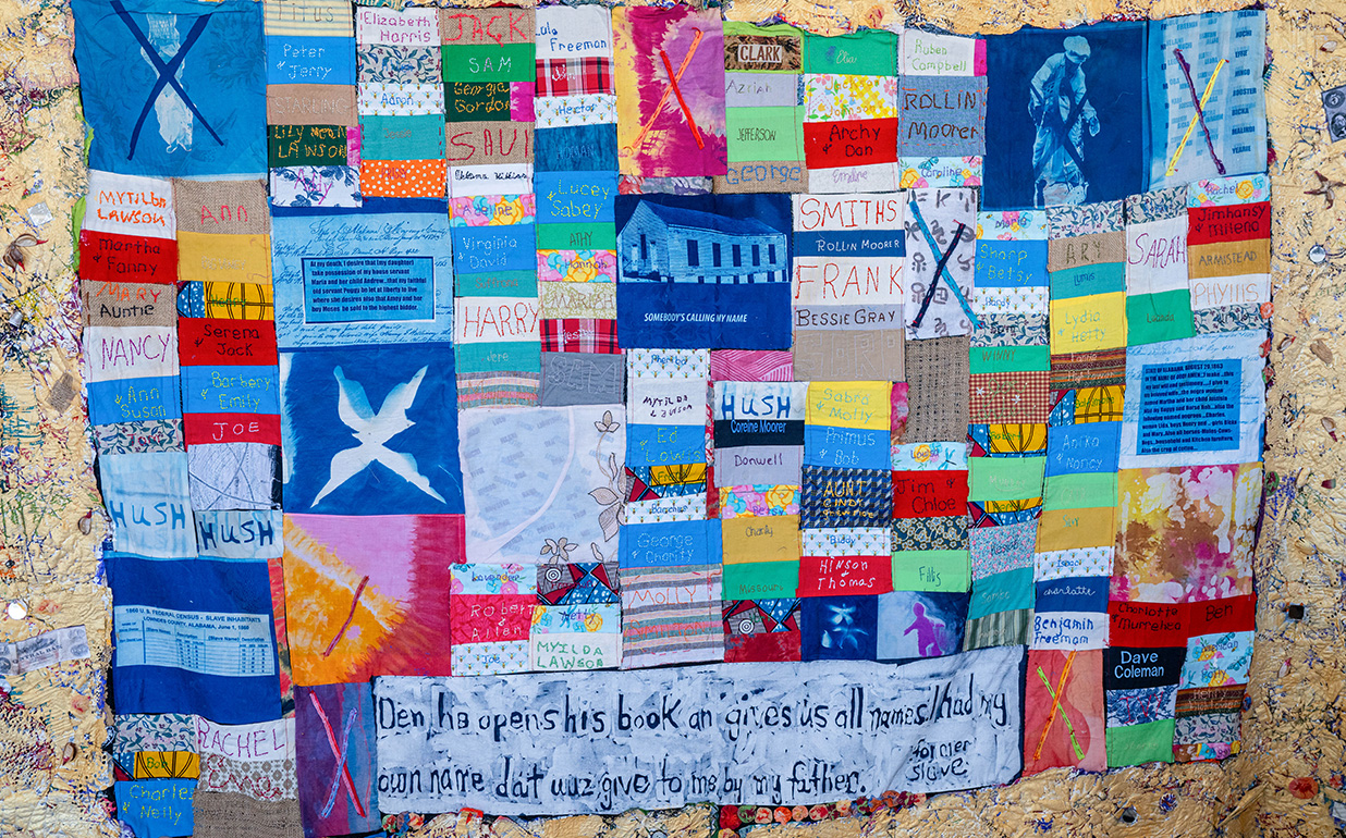A colorful patchwork quilt made of many small fabric squares, each with stitched names, drawings, patterns, and brief text, collectively forming a memorial-style artwork.