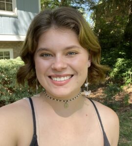 Selfie of Trinity Griffin. She has chin length brown hair and is wearing a black camisole and choker necklace