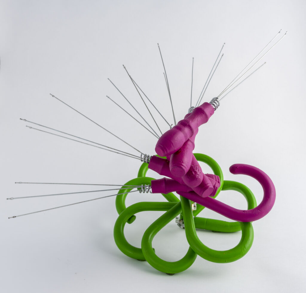 Eight disassembled umbrella frames without fabric, attached together in a a spiral. The top handle is painted bright pink and the remaining seven handles are painted bright green.