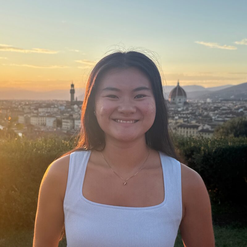 Lydia Rotta in Florence, Italy. Lydia has dark, long hair and wears a white tank top.