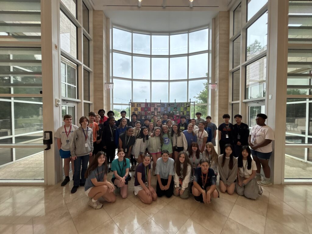 A group of students pose in front of the collaborative quilt in The Jule's lobby.