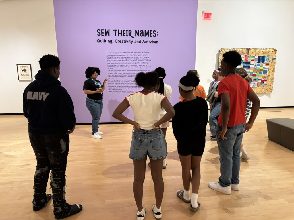 A Jule student guide leads seventh graders on a tour of the Sew Their Names exhibition.